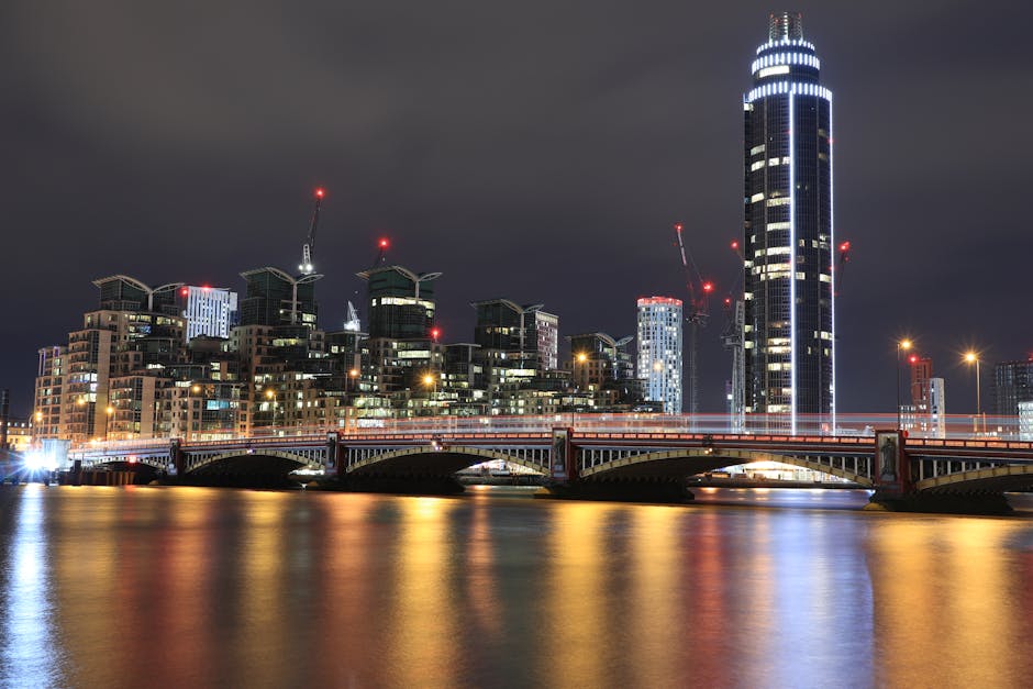 A wide view of the London skyline in the background, featuring numerous modern glass-clad skyscrapers and high-rise office buildings under a blue sky with scattered clouds. In the foreground, a docksi